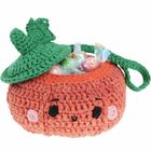 Eine gehäkelte, orangefarbene Tasche in Form eines Kürbisses mit einem freundlichen Gesicht und grünem Deckel, gefüllt mit Bonbons.