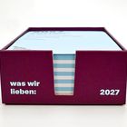 Die Texte "was wir lieben:" und "2027" stehen auf einer weinroten Box, die hellblaue Karten enthält.