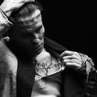 Der Text "HOPE" ist über der Brust tätowiert. Eine Schwarz-Weiß-Aufnahme zeigt eine Person mit Stichen am Kopf.