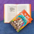 „In Our Own Words: True Stories of Indian Boarding Schools“. Ein Buch liegt auf einem geöffneten Buch mit Text über den Meriam Report.