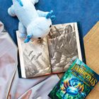 "The Last Immortals: Dawn of the Axolotl" Buch, ein hellblaues Plüsch-Axolotl, offene Seiten mit Illustrationen.