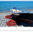 "Fischerboot am Strand" steht im Bild. Ein Boot liegt auf einem Kieselstrand, rote Netze darunter und blaues Meer im Hintergrund.