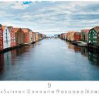 Trondheim, 9, 1-30, Casares Edition. Bunte Fassaden von Häusern entlang eines Flusses unter bewölktem Himmel.
