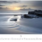 CASARES EDITION unten links, große graue 9 in der Mitte. Ein ruhiger Strand bei Sonnenaufgang, mit Felsen und Spuren im Sand.