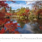 09, CASAES EDITION. Ein ruhiger See mit einer kleinen Brücke umringt von roten Herbstbäumen unter blauem Himmel.