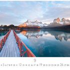 „Morgenstimmung“ zeigt eine Brücke zu einem roten Haus am See, umgeben von schneebedeckten Bergen unter einem bewölkten Himmel.