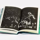 Text auf der rechten Seite, darunter ein schwarz-weiß Foto von einer Person auf einer Bühne vor Publikum.