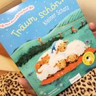 "Träum schön, kleiner Schatz" steht auf einem blauen Cover mit schlafenden Schafen und einem Kätzchen auf einer Wiese.