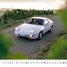 Kalenderblatt mit Datum unten. Weißes Auto fährt auf einer Straße durch Weinberge bei Sonnenuntergang.