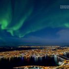 "Die beste Zeit für Nordlichter in Tromsø ist von September bis April." Grüne Nordlichter über einer erleuchteten Stadt.