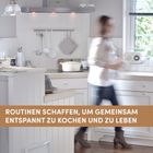 Text: "ROUTINEN SCHAFFEN, UM GEMEINSAM ENTSPANNT ZU KOCHEN UND ZU LEBEN." Eine moderne, helle Küche mit vielen Utensilien.
