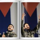 Ein Mann mit Bart in olivgrüner Uniform spricht energisch vor mehreren Mikrofonen, mit erhobenen Händen. Im Hintergrund eine rot-blaue Flagge.