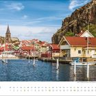 September-Kalenderbild: Malerisches Küstendorf mit bunten Holzhäusern, einem Kirchturm und Felsen am Wasser.