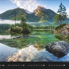 09,  Kalenderdaten: 01 bis 30. Bergsee mit Bäumen, spiegelndes Wasser, Berge im Hintergrund, blauer Himmel, leichte Wolken.