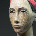 Sorgil Iontarai. Eine geschnitzte Büste mit ausdrucksstarken Augen und einem rot-schwarzen Kopftuch auf dunklem Hintergrund.