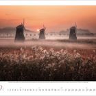 9, 2023. Kalenderblatt mit drei Windmühlen im Nebel bei Sonnenaufgang, umgeben von hohem Gras.