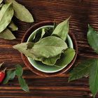 Keine Texte vorhanden. Trockene Lorbeerblätter in Schalen auf Holz, frische Blätter und rote Chili-Schoten daneben.