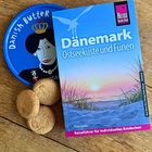 "Reise Know-How Dänemark Ostseeküste und Fünen" Reiseführer neben Keksdose mit "Danish Butter" und illustriertem Porträt.
