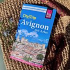 Reiseführer "City|Trip Avignon mit Arles" auf Strohhut, mit Sonnenbrille und lavendelfarbenen Blüten daneben.