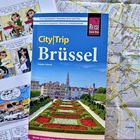 "CityTrip Brüssel". Reiseführer mit Stadtansicht, umgeben von Comics und einer Landkarte im Hintergrund.