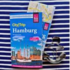 Auf einem blau-weiß gestreiften Tuch liegt ein Hamburg-Reiseführer mit Karte und eine Anker-förmige Plätzchenform.