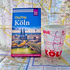 „CityTrip Köln“ Reiseführer vor Stadtplan, Köln-Tasse mit Karte als Muster.