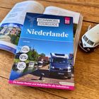 "WOHNmobil Tourguide Niederlande" steht auf einem Reiseführer, daneben ein Modellauto und aufgeschlagenes Buch.
