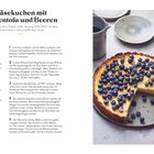 Titel: Käsekuchen mit Seidentofu und Beeren. Eine Scheibe fehlt, der Kuchen ist mit vielen Heidelbeeren garniert.