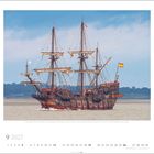 9 2027. Großes Segelschiff mit mehreren Masten auf einem Fluss, spanische Flagge, bewölkter Himmel im Hintergrund.