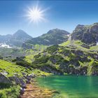 Juli-Kalender und Text über die Hohe Tatra. Berglandschaft mit klarem See, grünen Hängen und strahlendem Sonnenschein.
