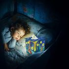 Text "non fiction". Ein Kind schläft mit Locken im Bett, daneben ein leuchtender Würfel mit Nacht-Illustrationen.