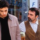 Zu sehen sind die Buchstaben "OFRA" auf einer Glasoberfläche. Zwei Männer stehen nah beieinander, der jüngere schaut nach unten.