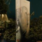 Ein Buchrücken zeigt „Die Antwort ist“ und „Emilia S.“. Eine Nahaufnahme einer Frau ist auf dem Cover, umgeben von Pflanzen.
