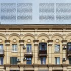 Text links: "axes') for being structured to a rhythm...", "‘monumentality’ of architectural...", "a finely profiled cornice, set high on..." Rechts in vertikaler Schrift: "The garden cities Paivayny and Aeroflot". Weiterer Text in kyrillischer Schrift ist marginal zu erkennen.  
Das Bild zeigt eine Mehrfamilienhausfassade mit dekorativen Ornamenten, Balkonen und Klimaanlagen.