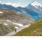 „September.“ Ein Radfahrer erklimmt einen Bergpass, umgeben von kargen Wiesen und schneebedeckten Bergen.