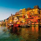 Farbenfrohe Boote und Gebäude am Flussufer; sonnige Beleuchtung, klare blaue Himmelsansicht. Lebendige, geschäftige Szene.
