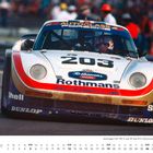 Text „203 Rothmans Porsche“ auf Rennwagen. Kalender zeigt September. Fahrer mit Helm im Cockpit. Zuschauer im Hintergrund.
