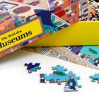 Text: "Die Welt des Museums". Eine offene Puzzle-Verpackung, Puzzleteile liegen auf dem Tisch. Illustrationen von Museumsbesuchern.