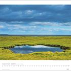 September 2027 | Inseln & Meer. Grünlandschaft mit Wasserfläche unter bewölktem Himmel.