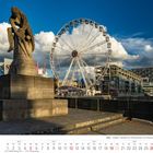 Köln – Skulptur Tauzieher am Rheinufer. Ein großes Riesenrad und moderne Gebäude im Hintergrund, unter blauem Himmel.