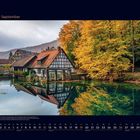 09 September. Fachwerkhaus am See mit Herbstbäumen in leuchtendem Orange und Gelb, spiegeln sich im Wasser.