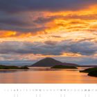 09. Mývatn, Skútustaðir, Norðurland eystra. Sonnenuntergang mit orange leuchtenden Wolken über einem ruhigen See und Hügeln.