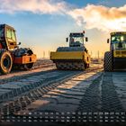 Ein Kalender mit Monatsübersicht. Drei schwere Baumaschinen stehen auf sandigem Boden im Sonnenuntergang.