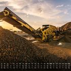 Kalender im September. Gelbe Maschine transportiert Steine auf einen Schutthaufen, Sonnenuntergang im Hintergrund.