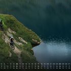 Kalenderblatt Oktober. Zwei Mountainbiker fahren einen schmalen Pfad entlang eines Sees.