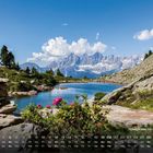 Text: "Spiegelsee mit Dachstein 9". Ein Bergsee mit Blumen, Felsen und Bergen darunter ein Kalender.