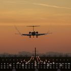 Kalender: September. Flugzeug landet bei Sonnenuntergang. Lichter markieren die Landebahn.