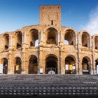 "Amphitheater von Arles 11." Bild zeigt ein historisches, steinernes Kolosseum mit Bögen unter einem klaren Himmel.