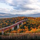 Herbstwald in Hokkaido, Japan mit rotem Viadukt, umgeben von bunten Bäumen und Bergen im Hintergrund.