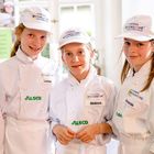 Drei Kinder in weißer Kochkleidung mit Aufschrift "Europa Miniköche", Namensschilder: Leonie, Melissa, Fernanda. 